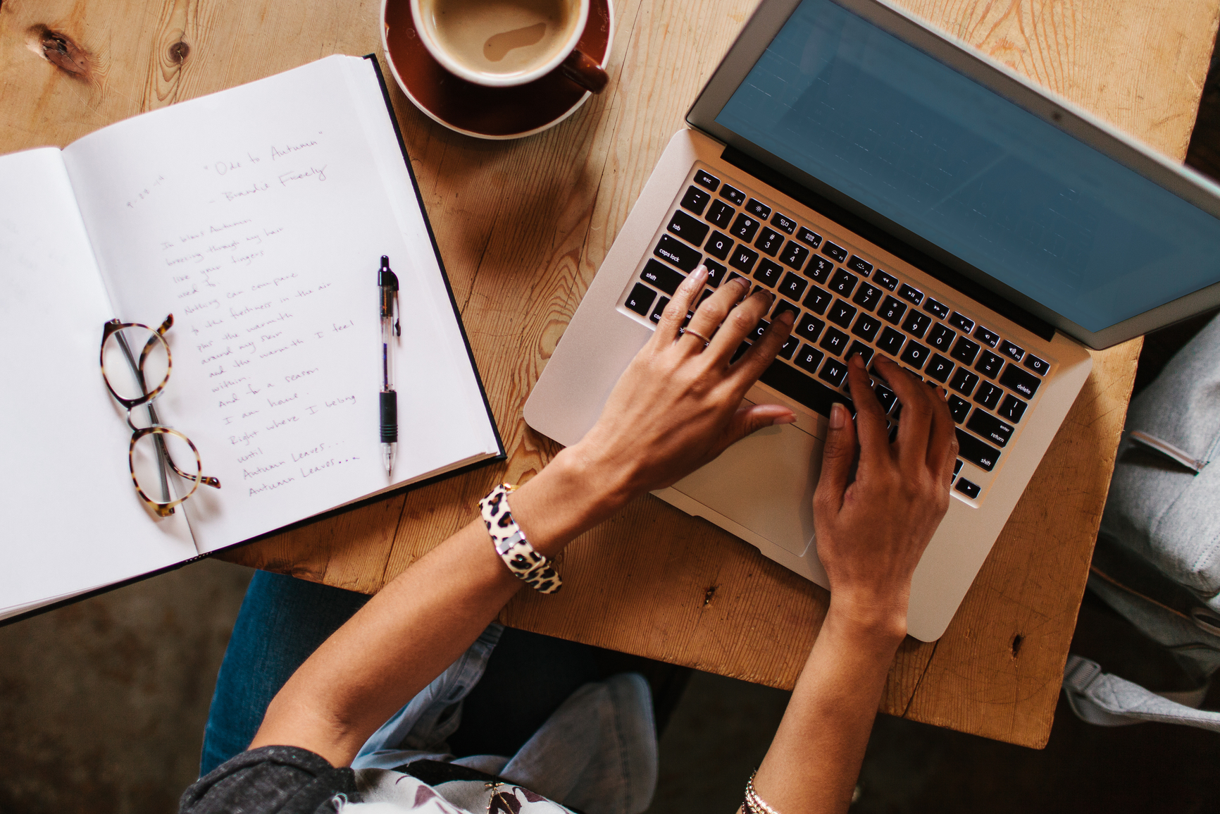 Woman sitting at a coffee shop working on a laptop and taking notes in a notebook.