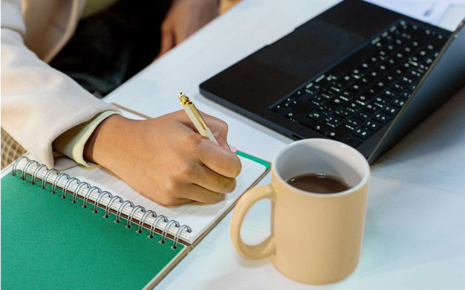 Close up of hand writing at laptop with coffee